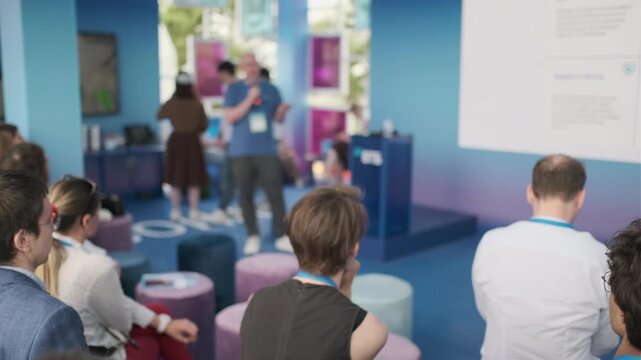 Group of people attending a presentation with screens showcasing multimedia visuals in bright venue.