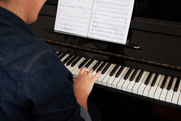 Person playing piano with open sheet music, practicing musical notes and chords indoors