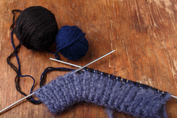Knitting needles, dark blue mohair and black acrylic yarn balls on old wooden table background....