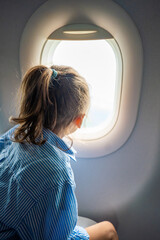 Little girl looking out the airplane window during a flight. Wonder, travel experience, and childhood curiosity in the air.