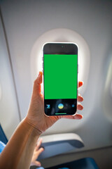 Close-up of a hand holding a smartphone with green screen camera active, recording view from airplane window. Travel content creation, mobile photography, and mockup preparation in flight