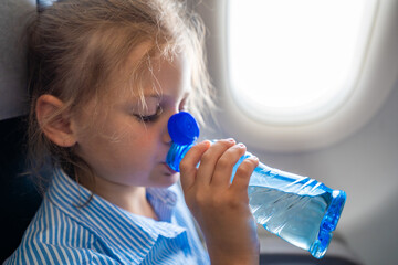 Little girl drinking water from a plastic bottle during a flight. In-flight hydration, travel routine, and caring for body needs while flying