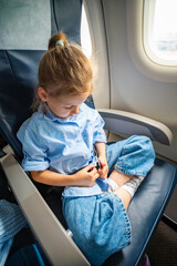 Little girl fastening her seat belt while sitting on an airplane. Family travel, flight safety, and...