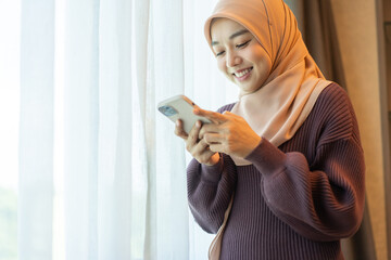 Asian muslim woman use smartphone at home, female in hijab checking messages, modern communication,...