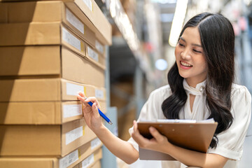 Asian warehouse staff woman checking inventory with clipboard in logistics management, working in...