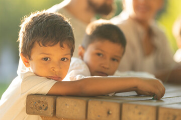 Pensive latin american brothers leaning on picnic table with family in background