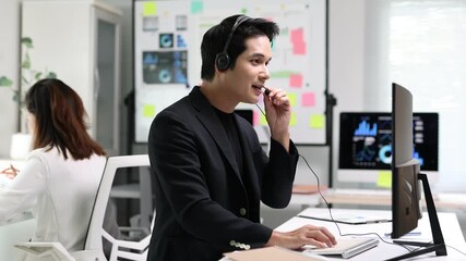 Professional businessman working at computer, wearing headset while communicating with colleagues in modern office, collaborative workspace. - Powered by Adobe