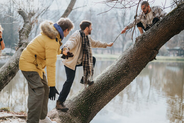 A group of friends collaborate to help each other balance across a fallen tree trunk over a calm...
