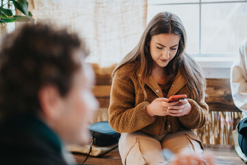 A young woman enjoys her time indoors, sitting comfortably, and concentrating on her phone screen....