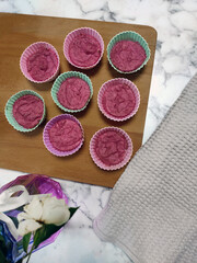 Pink and purple dough is laid out in silicone molds of pastel shades - blue, pink and purple. berry cake, neatly laid out on a wooden board, purple vase with a flower, home cooking
