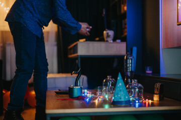 A person arranges a celebration table adorned with colorful lights, glassware, and decorations.