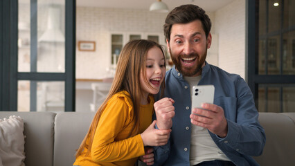 Happy smiling Caucasian family father man dad hold mobile phone child daughter winning scream rejoice male parent give high five little kid girl cuddle success victory at home great results happiness