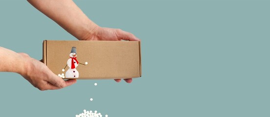 Paper box in hands. Artistic concept of winter season entertainment, holiday packages, shopping. Snowman and snowballs. Throwing a snowball. Cut out. Place for text. Sustainability and modernity