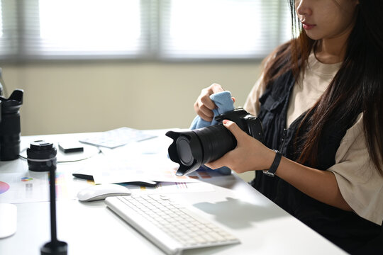Female photographer carefully cleaning a camera lens at her modern editing workspace
