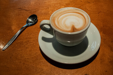 Freshly brewed white ceramic mug of hot, foamy cappuccino with decorative milk froth heart.