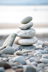 A vertical composition of smooth grey pebbles stacked in a balanced tower on a coastal shore, symbolizing calmness and harmony. High quality photo