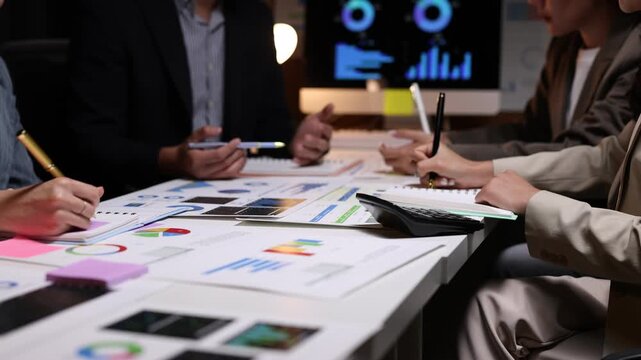 Professional business team analyzing financial charts and reports in office, collaborating under project deadline pressure while showcasing strategic problem-solving.