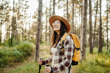 Young caucasian woman hiking or trekking through scenic forest with hiking sticks during golden hour