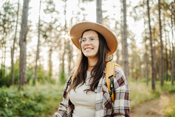 Young caucasian woman hiking or trekking through scenic forest with hiking sticks during golden hour
