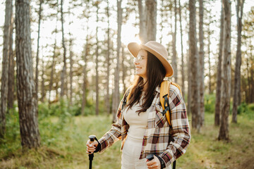 Young caucasian woman hiking or trekking through scenic forest with hiking sticks during golden hour