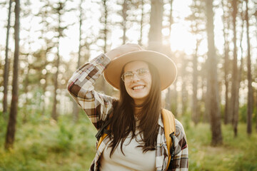 Young caucasian woman hiking or trekking through scenic forest with hiking sticks during golden hour