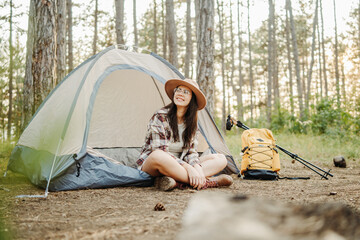 Young caucasian woman preparing tent and campfire in the scenic forest during golden hour