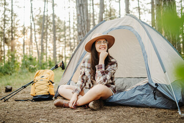 Young caucasian woman preparing tent and campfire in the scenic forest during golden hour