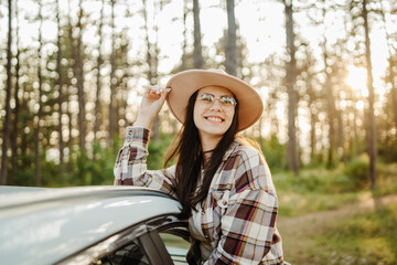 Young caucasian woman sitting on car window in the forest enjoying nature