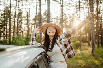 Young caucasian woman sitting on car window in the forest enjoying nature