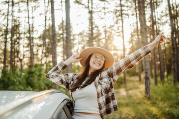 Young caucasian woman sitting on car window in the forest enjoying nature