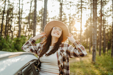 Young caucasian woman sitting on car window in the forest enjoying nature