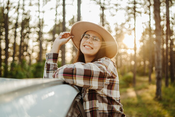 Young caucasian woman sitting on car window in the forest enjoying nature
