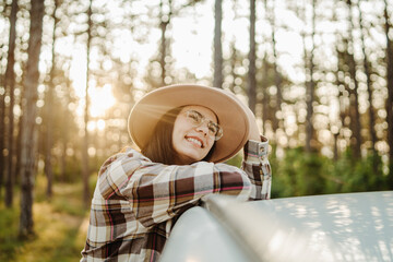 Young caucasian woman sitting on car window in the forest enjoying nature
