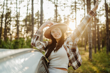 Young caucasian woman sitting on car window in the forest enjoying nature