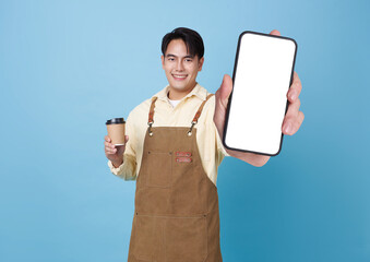 smiling Asian man in apron holds coffee cup and presents smartphone with blank white screen ideal...