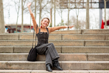 joyful woman sits on stone stairs with her arms stretched wide in a playful, carefree gesture