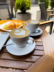 A white coffee cup of cappuccino on a wooden table with a plate of croissants. breakfast in cafe,...