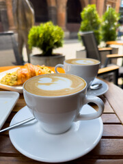 A white coffee cup of cappuccino on a wooden table with a plate of croissants. breakfast in cafe,...