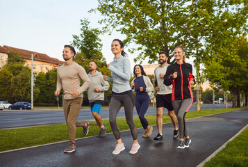 Outdoor shot of active young people running together along road, dressed in sportswear, having...