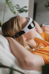 Woman relaxes with smart massage device on eyes at home, showing wellness, calm, mindfulness, recovery, digital care, technology, Gen Z lifestyle, comfort, balance, recharge, rest, breathing.