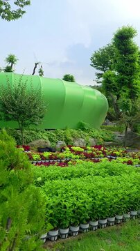 A unique leaf-shaped green glamping pavilion blends into a vibrant garden landscape with rows of potted plants and lush trees at Glamtree Resort in Gapyeong, South Korea.