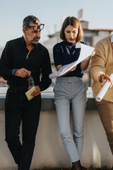 A diverse group of business people reviewing project plans outdoors. The team is engaged and...