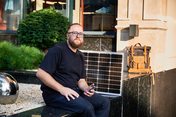 Bearded man using smartphone next to photovoltaic solar panel. Integration of sustainable renewable...