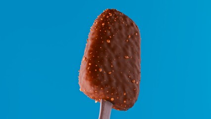 Frozen dessert bar fully coated in thick chocolate and embedded with nut bits, rendered in high detail. Displayed on a vivid blue background for high contrast. Suitable for food promotions, packaging