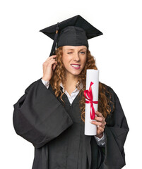 Graduate redhead with diploma covering ears with hands.
