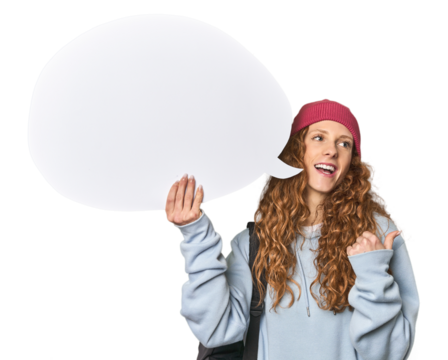 Redhead holding a comic speech bubble points with thumb finger away, laughing and carefree.