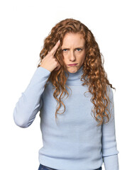 Simple redhead studio portrait frowning face in displeasure, keeps arms folded.