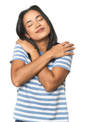Young Latina posing in studio hugs, smiling carefree and happy.