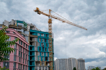 Tower crane against the sky, a brightly colored house is being built nearby