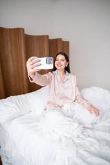 Peaceful woman using phone while sitting comfortably on bed